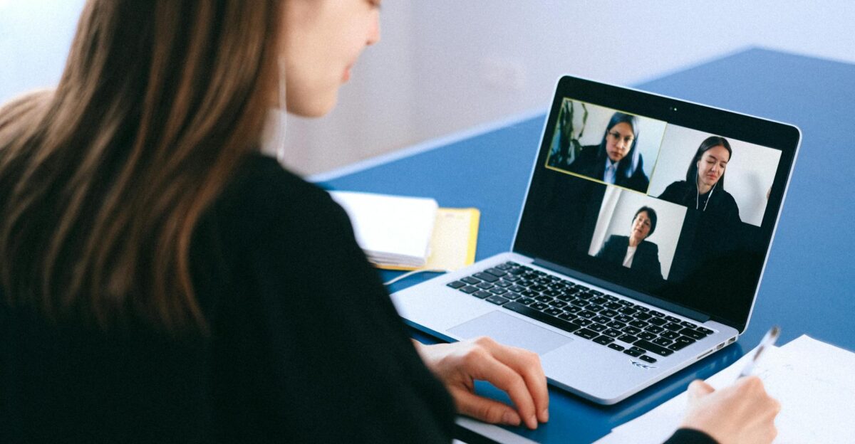 A woman engaging in a video conference using a laptop at home taking notes