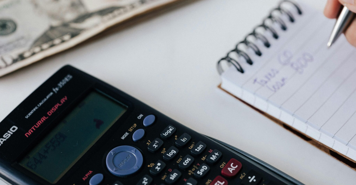 Close-up of a calculator, US dollar bill, and a hand writing in a notebook, symbolizing financial planning.