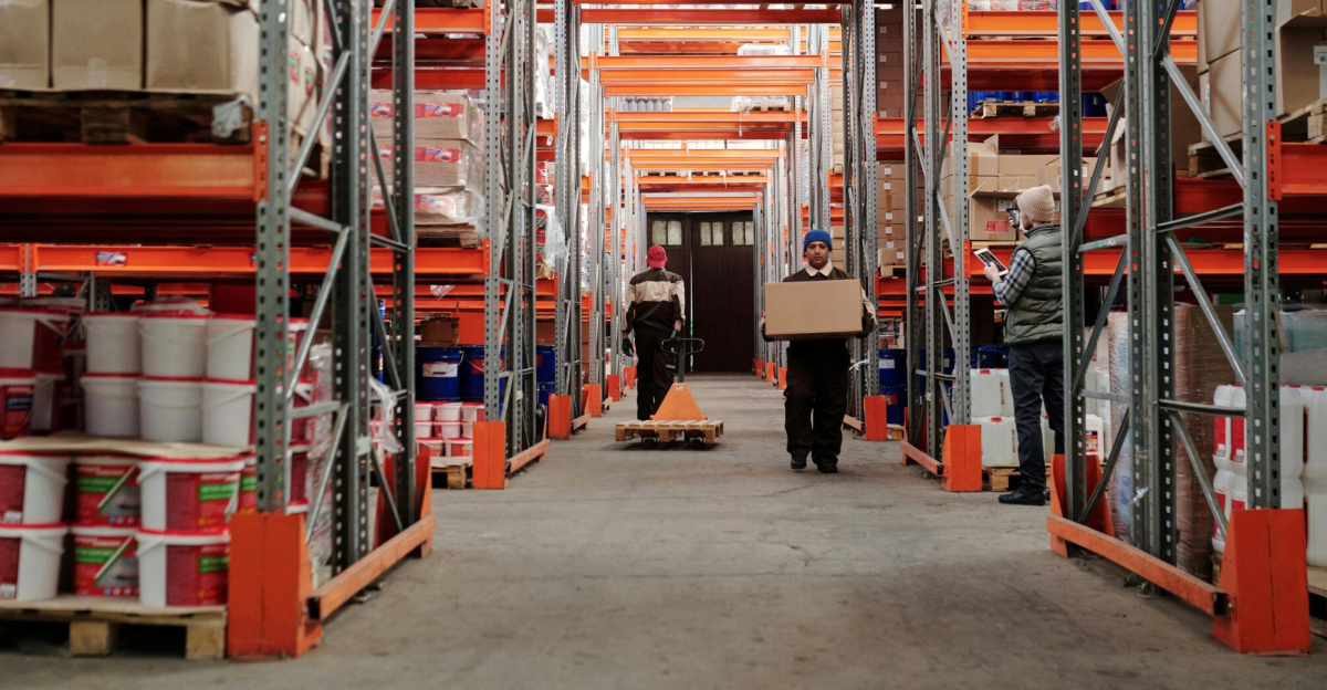 Warehouse interior showing workers handling boxes and organized shelves filled with products.