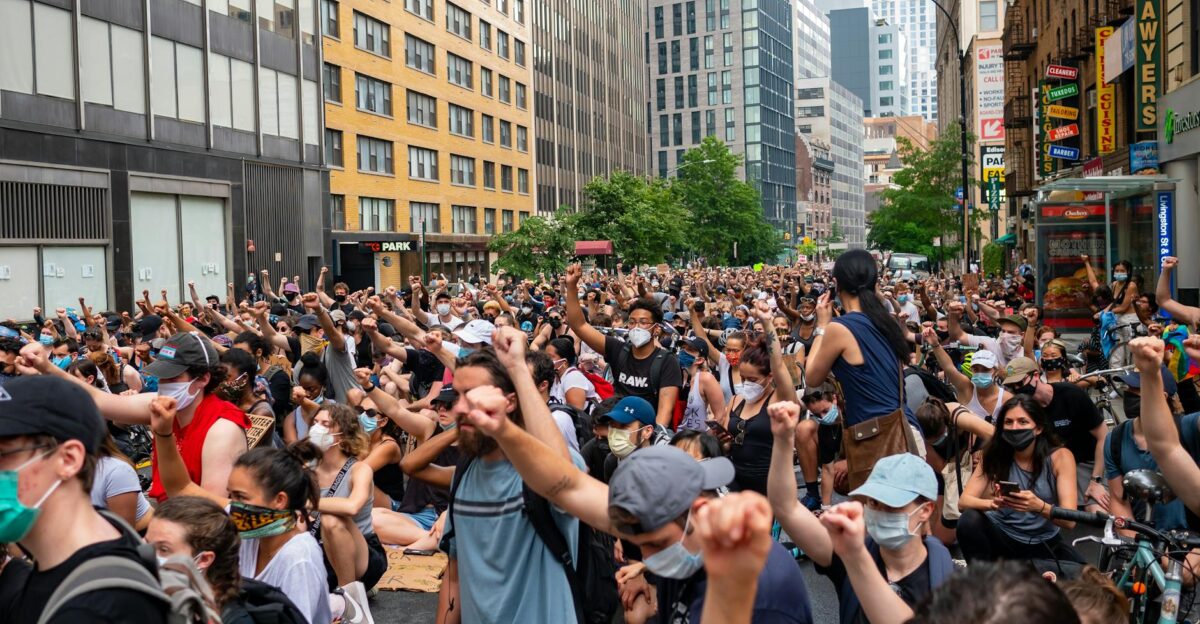 A large crowd of diverse protesters raising fists in a city street during daytime