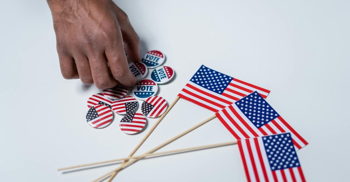 A hand reaches for voting buttons and American flags on a white background