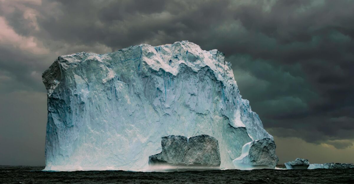A massive iceberg floating in the sea with dramatic storm clouds overhead showcasing nature s power
