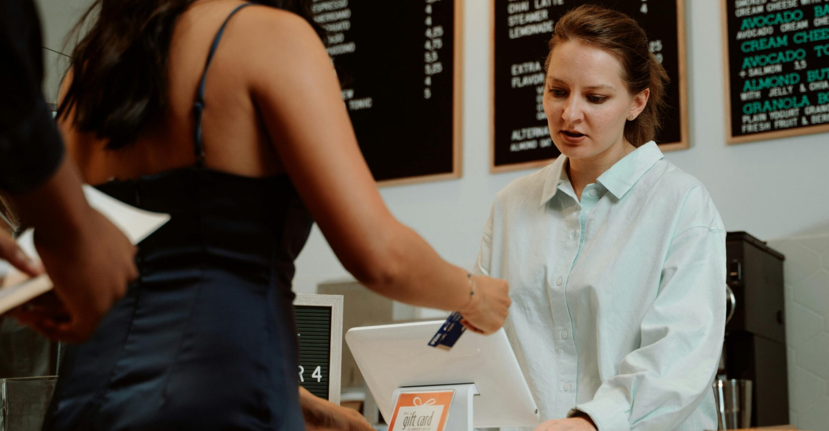 A customer pays with a card at a coffee shop as a barista assists.