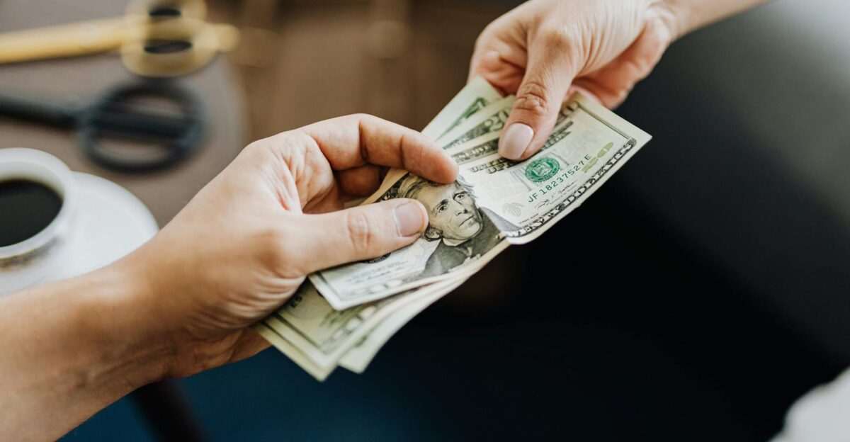 A close-up image of hands exchanging US dollar bills symbolizing financial transaction or payment