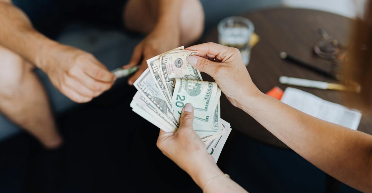 Close-up of people handling and counting US dollar bills indoors