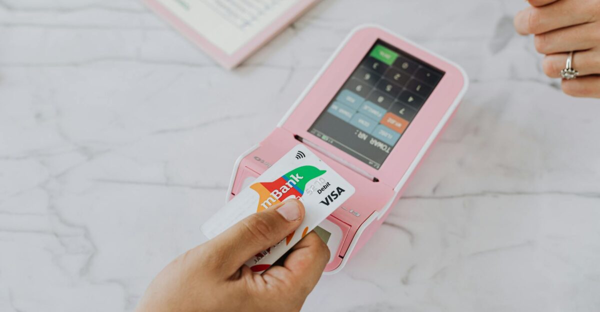 Hand using a contactless card on a pink POS terminal for a wireless transaction
