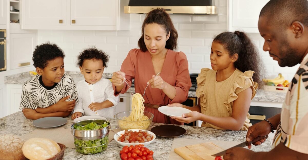 Family enjoying a cooking session together in a modern kitchen preparing pasta and vegetables