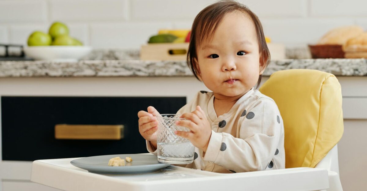 Adorable toddler sitting in a high chair enjoying a meal and drink inside a cozy kitchen