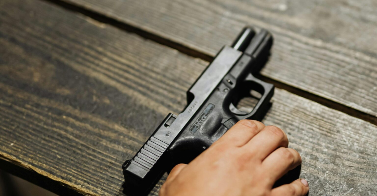 Close-up of a hand holding a handgun on a wooden table with bullet casing.
