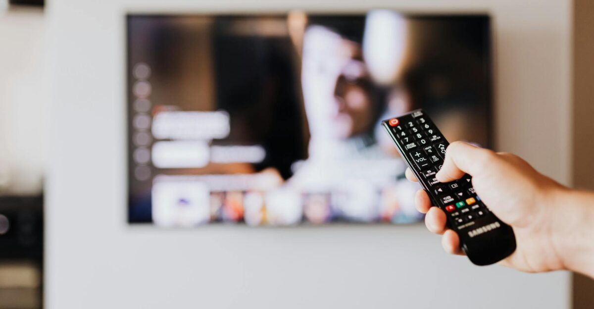 Person using a TV remote control with a blurred television screen in the background