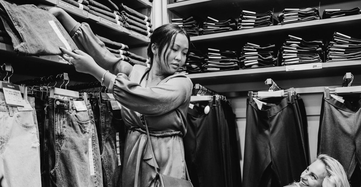 Two women shopping for jeans in a store, showcasing various fashion styles in a monochrome setting.
