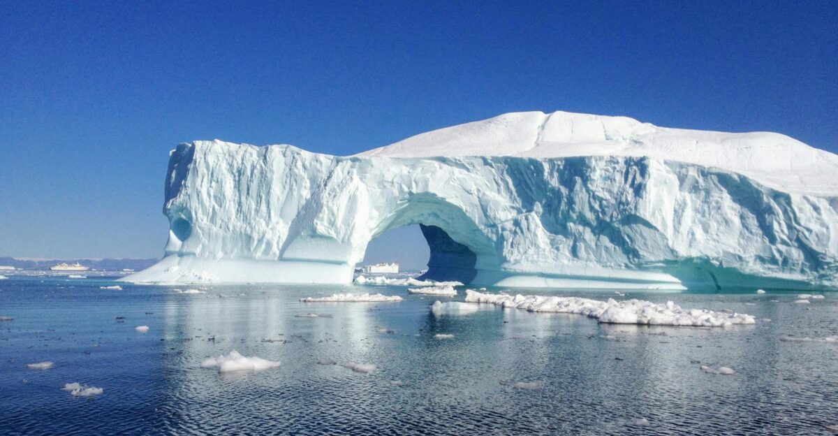 Majestic iceberg arch reflecting in the clear waters of Greenland s ocean under a bright blue sky