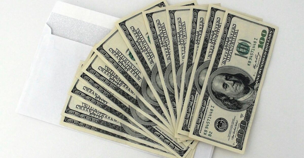 Fan of US 100 bills partially out of a white envelope on a white background