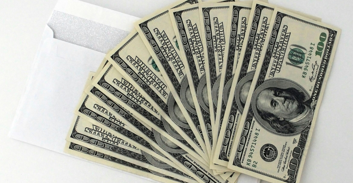 Fan of US $100 bills partially out of a white envelope on a white background.