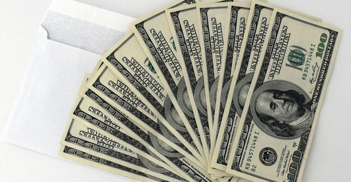 Fan of US $100 bills partially out of a white envelope on a white background.