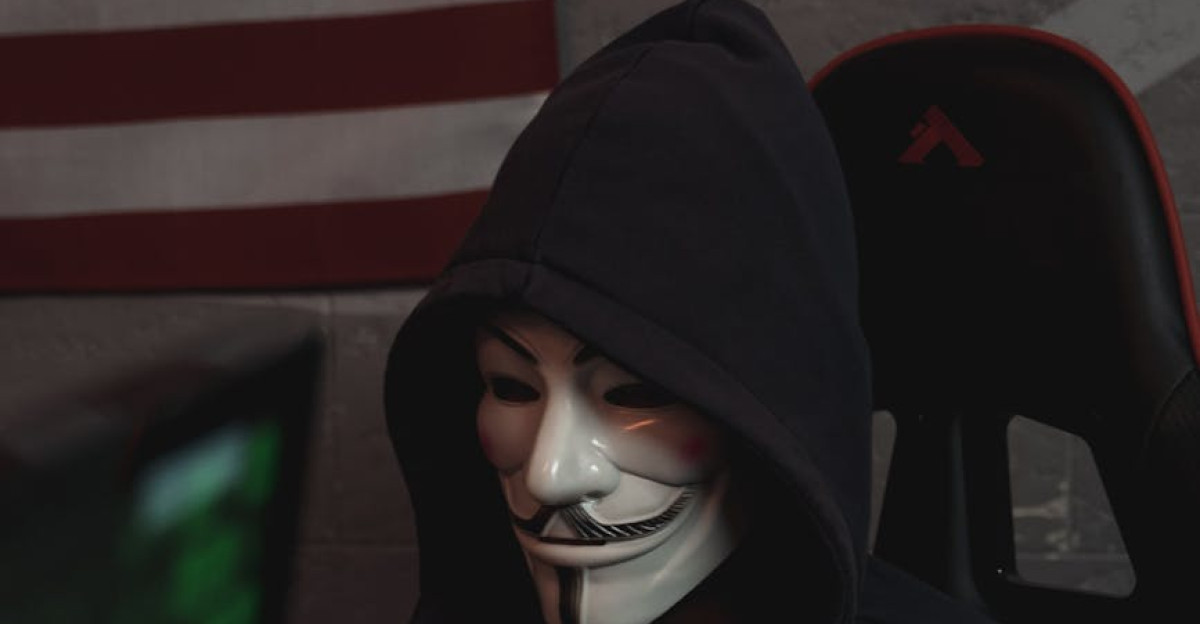 Masked hacker wearing a Guy Fawkes mask operates a computer symbolizing cyber security threats