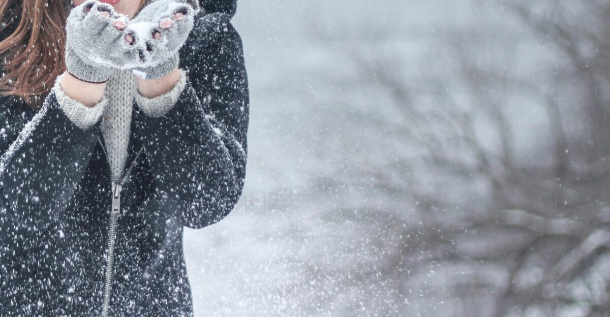 Woman in cozy winter clothing blowing snowflakes with excitement outdoors in a snowy setting