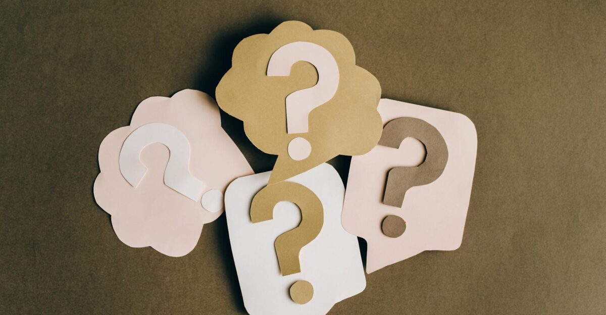 Four paper cutouts of question marks in beige and white on a brown surface symbolizing inquiry and curiosity