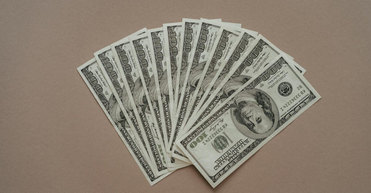 A neat arrangement of US dollar banknotes laid out in a fan shape on a brown surface