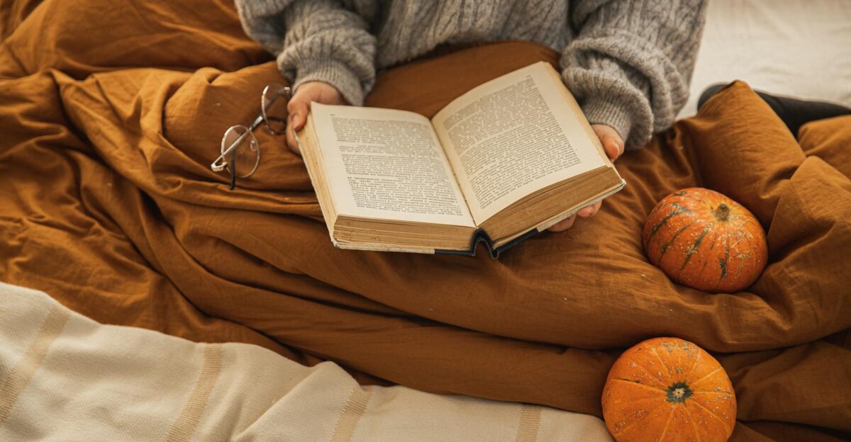 A person reading a book in a cozy setting with pumpkins embodying autumn relaxation