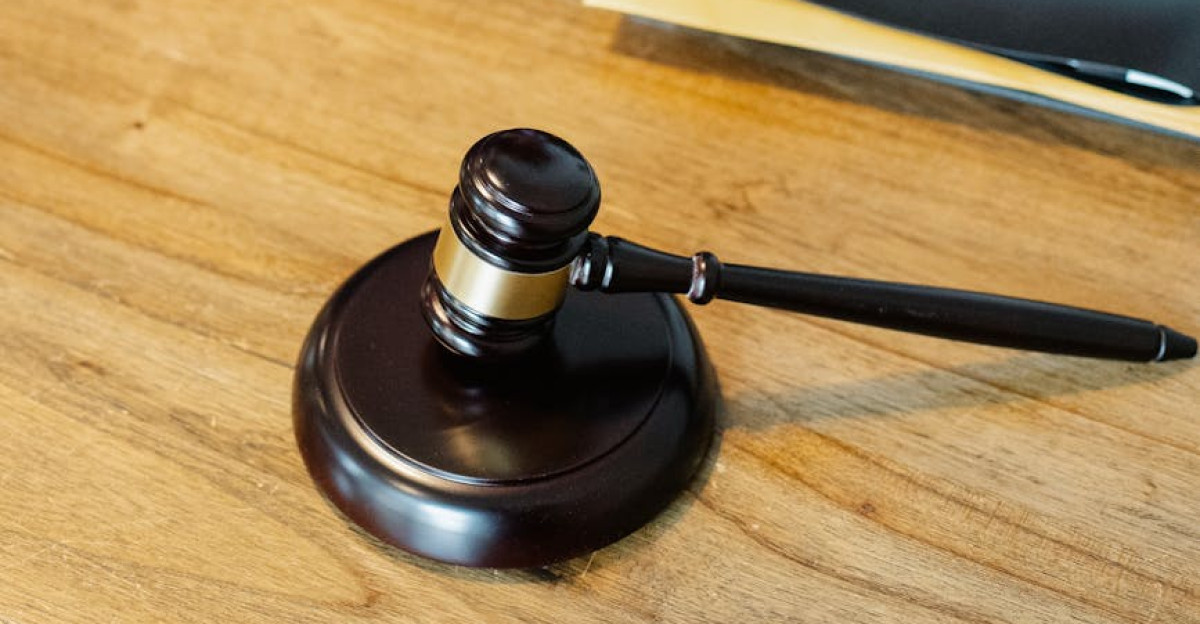 From above of crop anonymous male lawyer in formal clothes typing on laptop while sitting at wooden table with stack of documents and gavel
