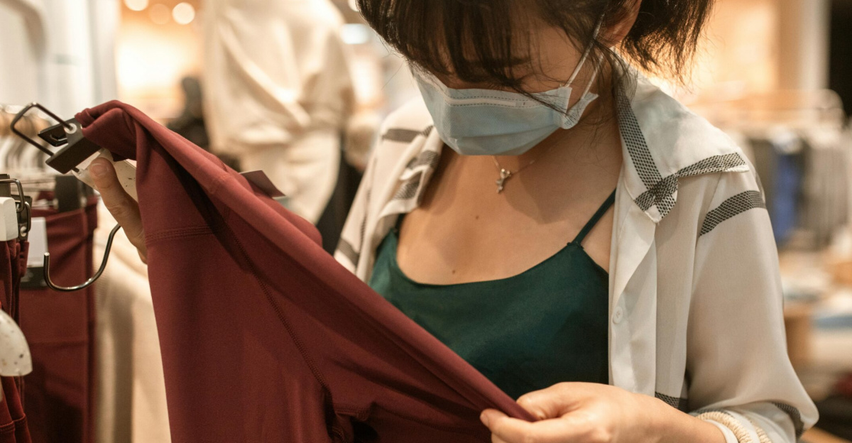A woman shops indoors wearing a face mask, examining clothes during the pandemic era.