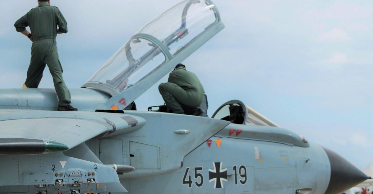 Low angle of unrecognizable male pilots in uniforms standing on aged gray multirole combat aircraft before flight against cloudy sunset sky