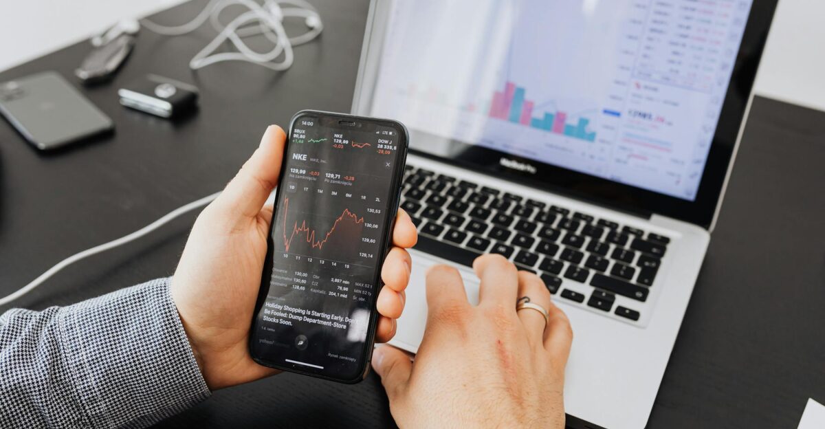 Person analyzes stock data with a smartphone and laptop indoors