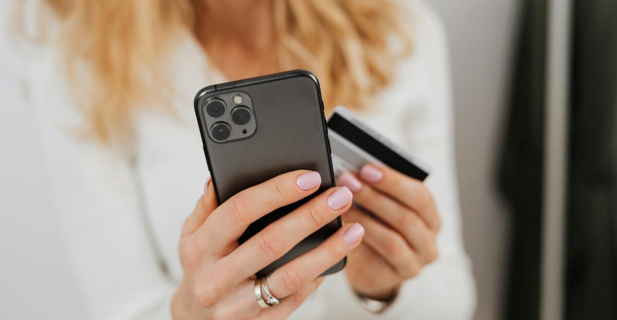 Close-up of woman holding smartphone and credit card for online transaction indoors