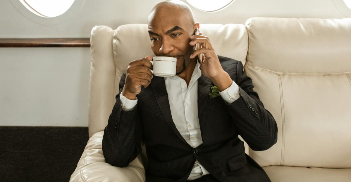 Elegant businessman seated in private jet drinking coffee and on a phone call