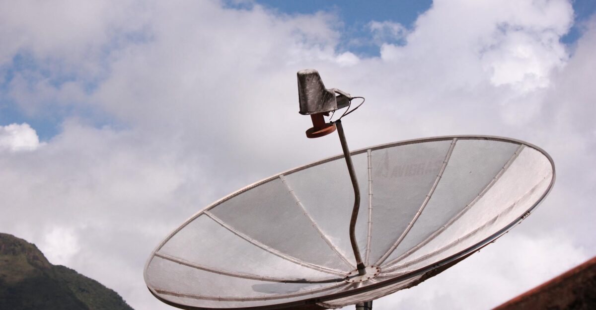 Silver satellite dish pointing skyward under a bright blue sky with scattered clouds
