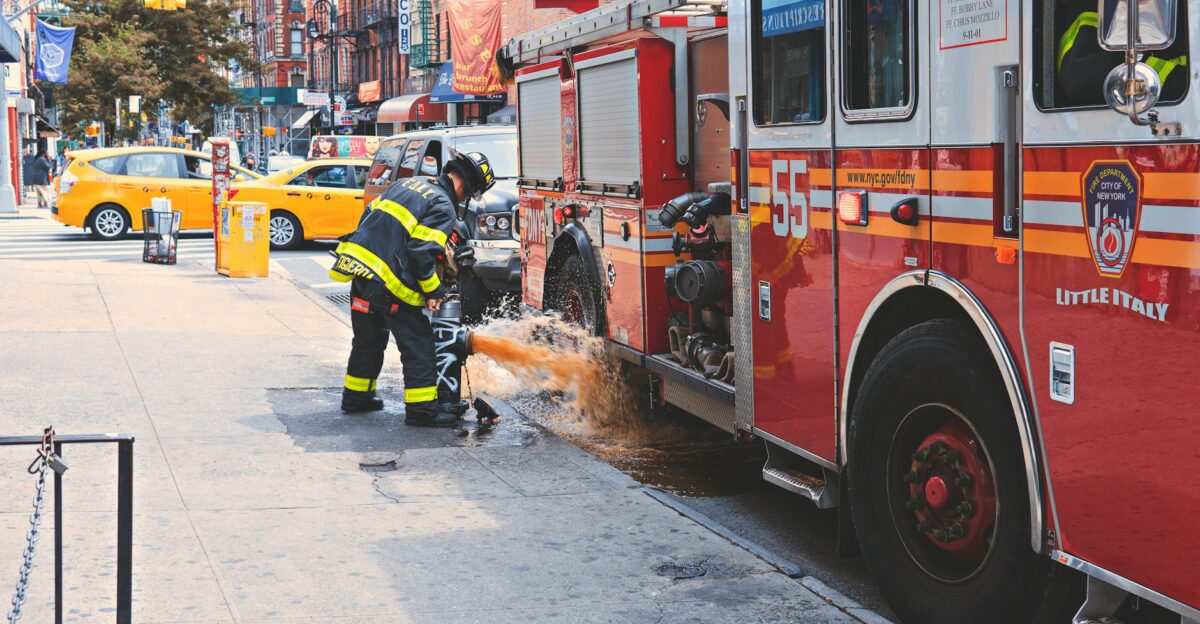 Firefighter handling hydrant beside fire truck on New York street with yellow taxi nearby