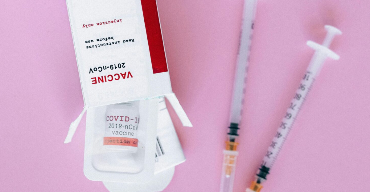 COVID-19 vaccine box and syringes arranged on a pink surface, symbolizing vaccination efforts.