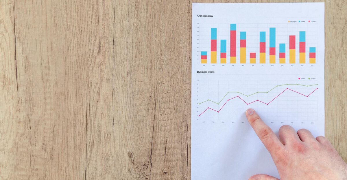 Hand analyzing business graphs on a wooden desk focusing on data results and growth analysis