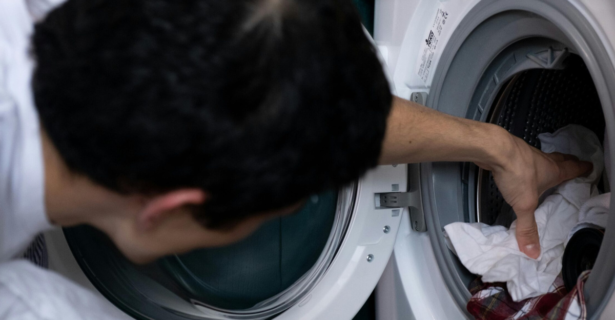 Close-up of a man placing clothes into a washing machine during household chores.