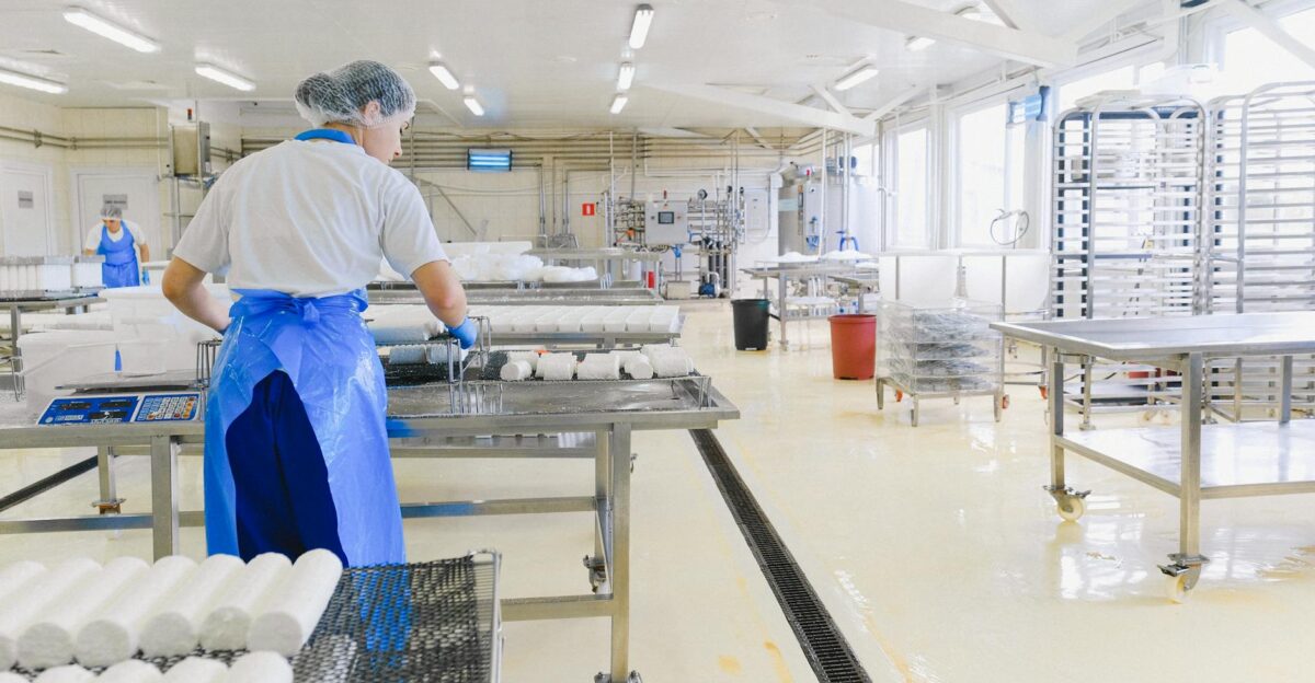 A worker in protective gear handles cheese in a modern dairy factory setting