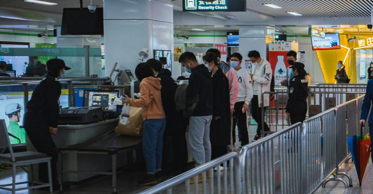 Travelers passing through airport security with staff and metal railings visible.