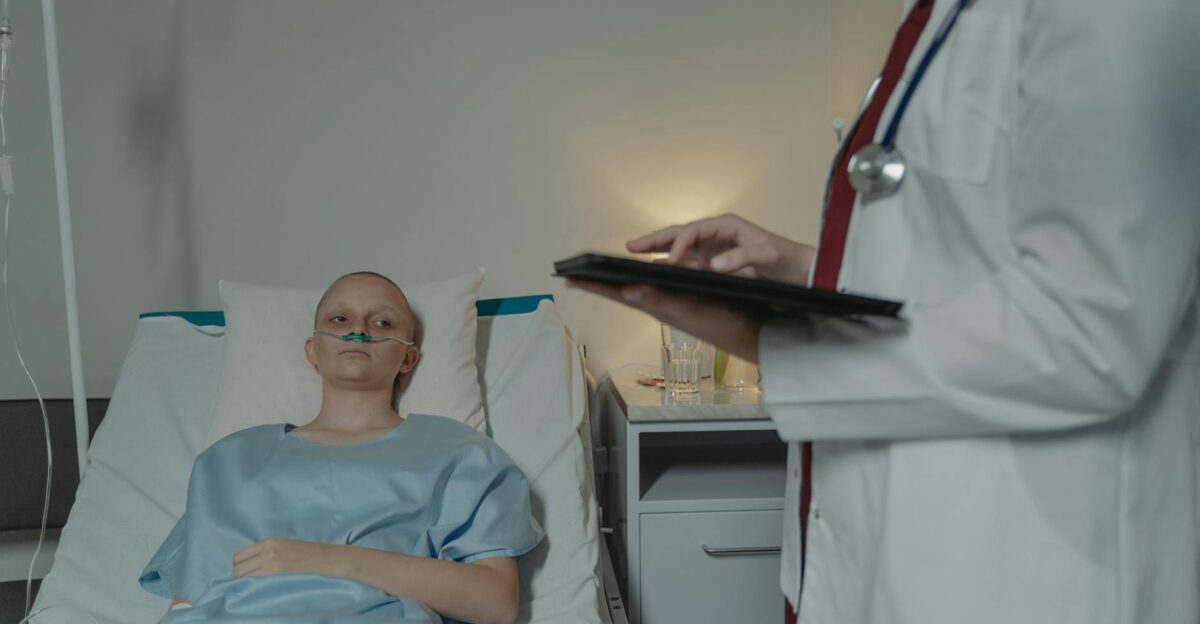 Woman in hospital gown lying in bed doctor checks digital tablet nearby