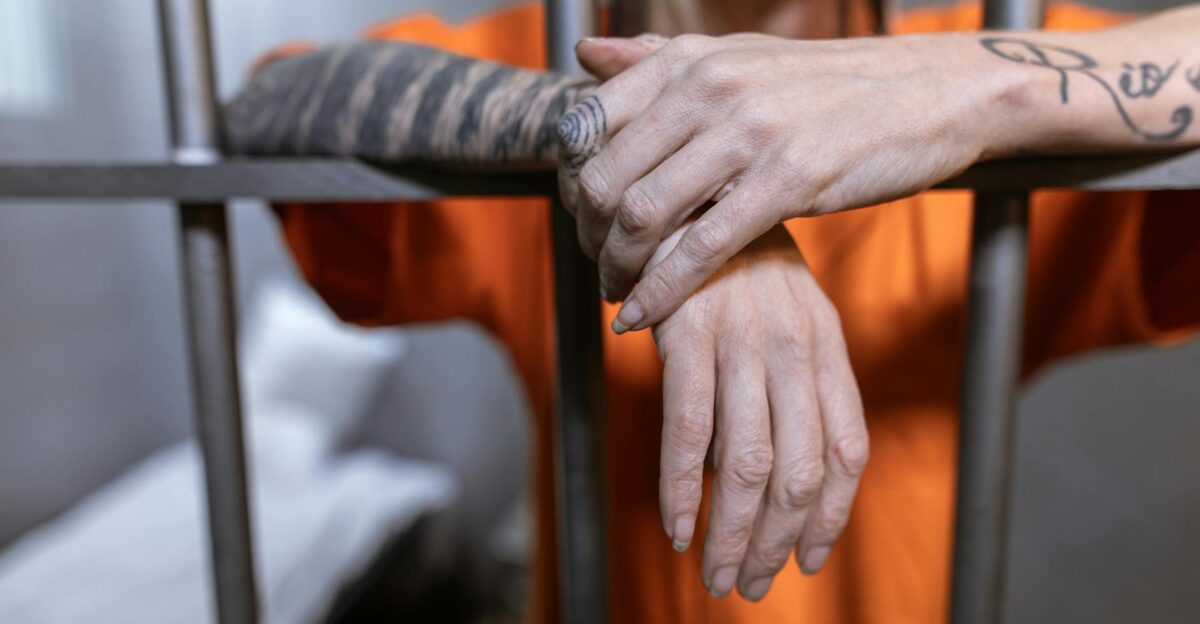 Close-up of tattooed hands behind jail bars illustrating incarceration and confinement