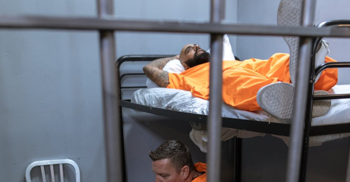Two inmates in a jail cell one resting on a bunk bed showcasing prison life