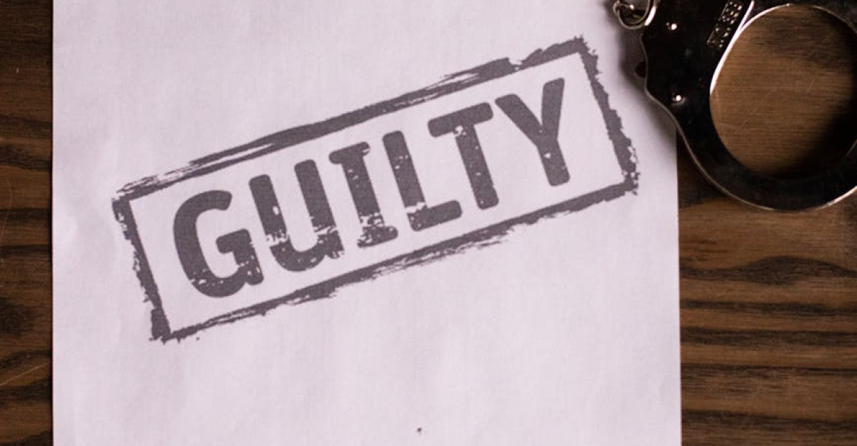 A close-up of handcuffs and a Guilty stamped document on a wooden table symbolizing law and justice