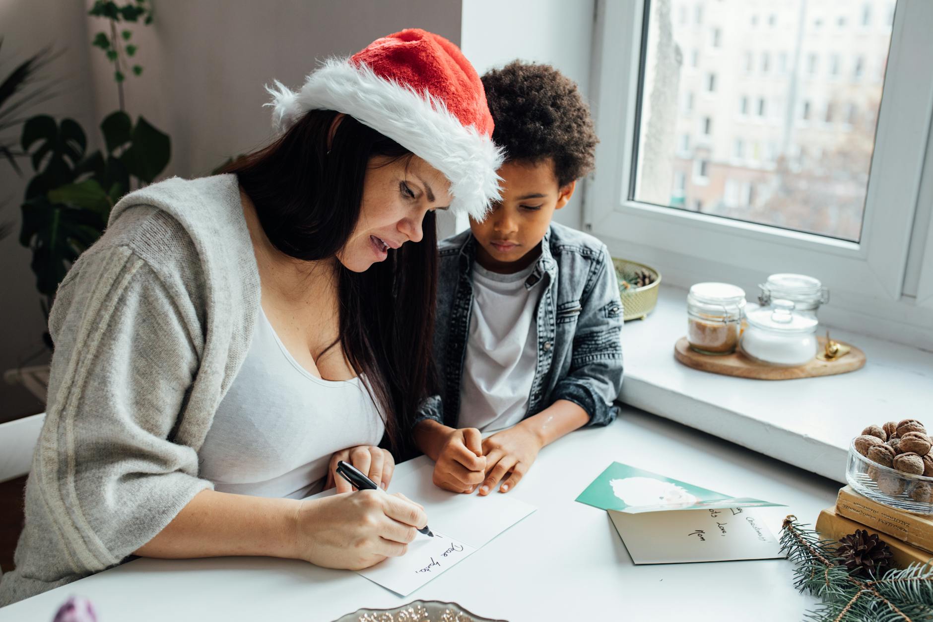 A mother and her son enjoy a festive moment writing Christmas cards by a window