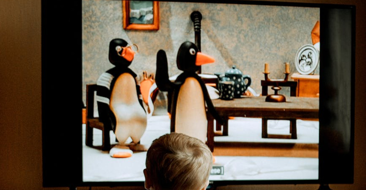 A toddler in colorful pajamas watches an animated penguin show on television indoors