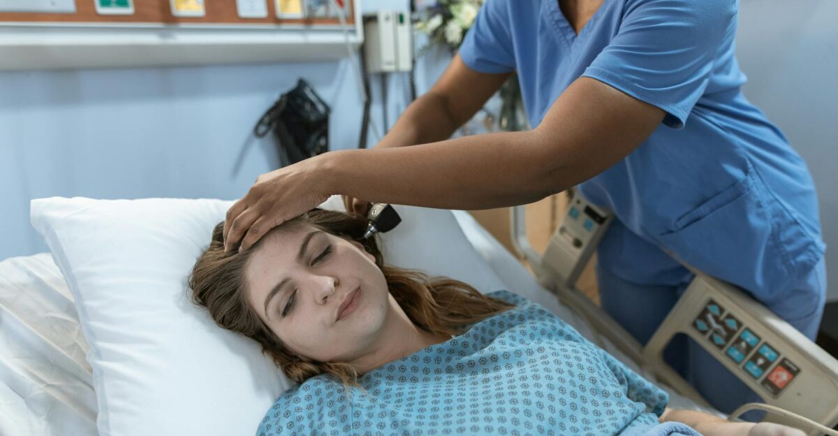 Crop African American female doctor with professional equipment doing examination of ear of woman lying on bed in hospital ward