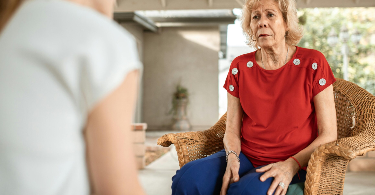 Senior woman in red shirt conversing indoors with younger woman. Daytime scene.