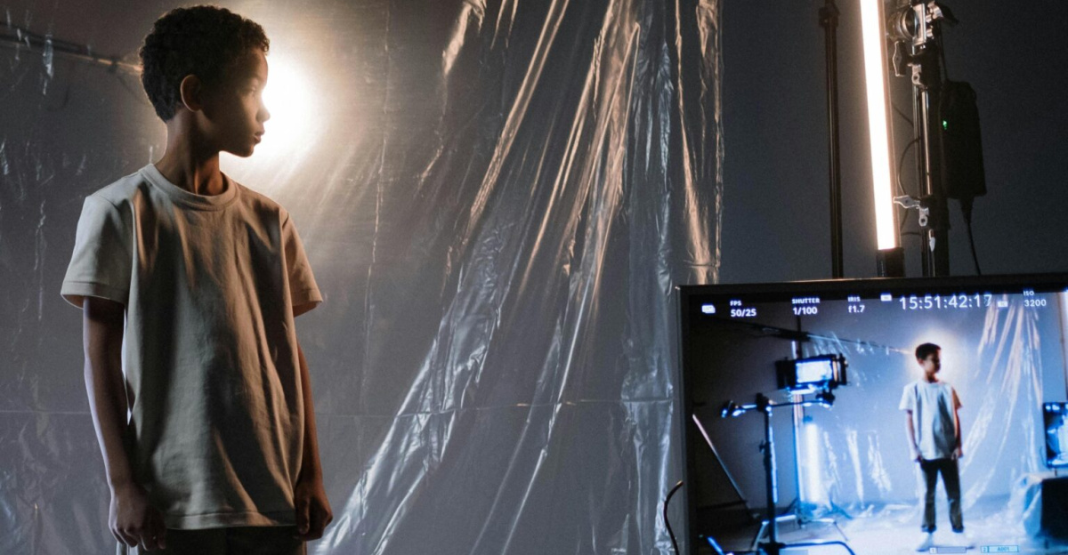 A young boy stands in a film studio surrounded by cameras and screens under soft lighting.