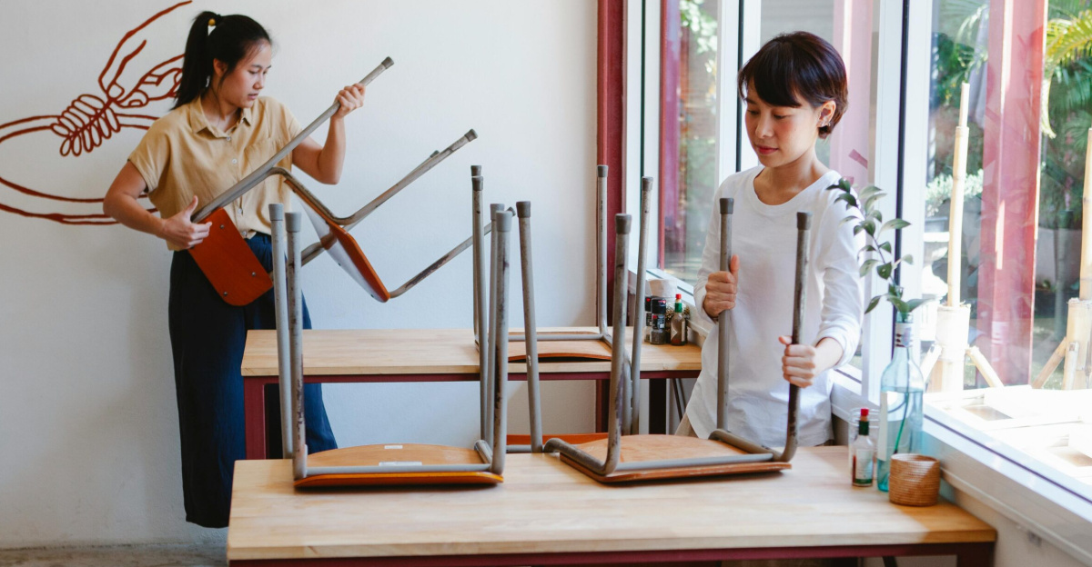 Two Asian women preparing a café for the day, arranging tables and chairs.