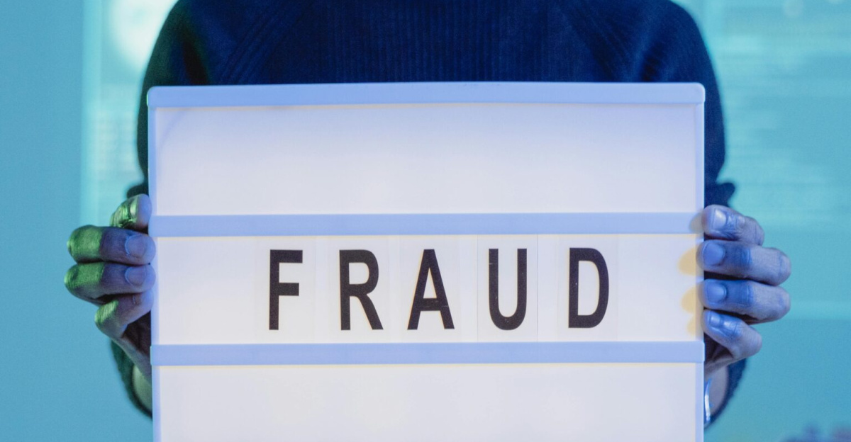 A man holding a sign reading 'FRAUD' in a tech environment, highlighting cybersecurity concerns.