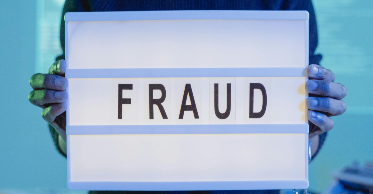 A man holding a sign reading 'FRAUD' in a tech environment, highlighting cybersecurity concerns.
