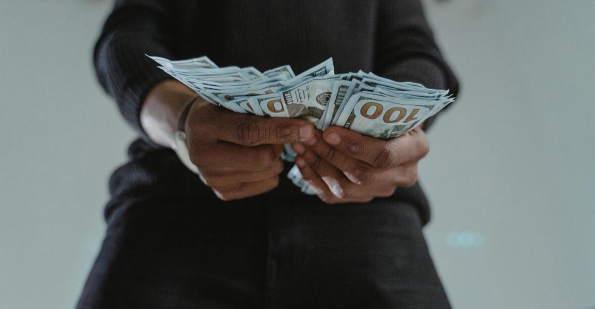 A close-up view of a person holding a stack of US hundred dollar bills indoors